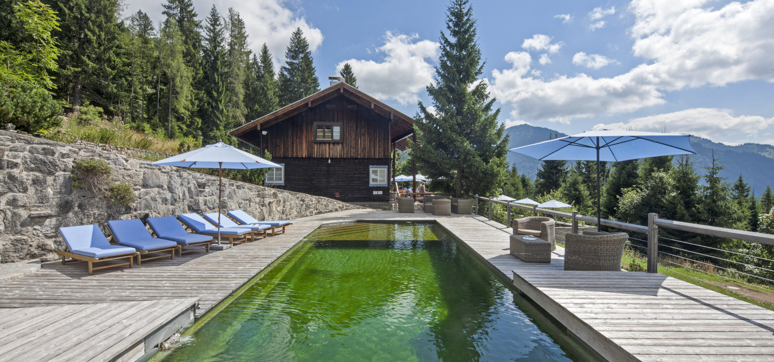 Naturpool mit Balena-System mit Liegen des Hotelbad „Silberghaus” in Bayrischzell, im Hintergrund die Alpen