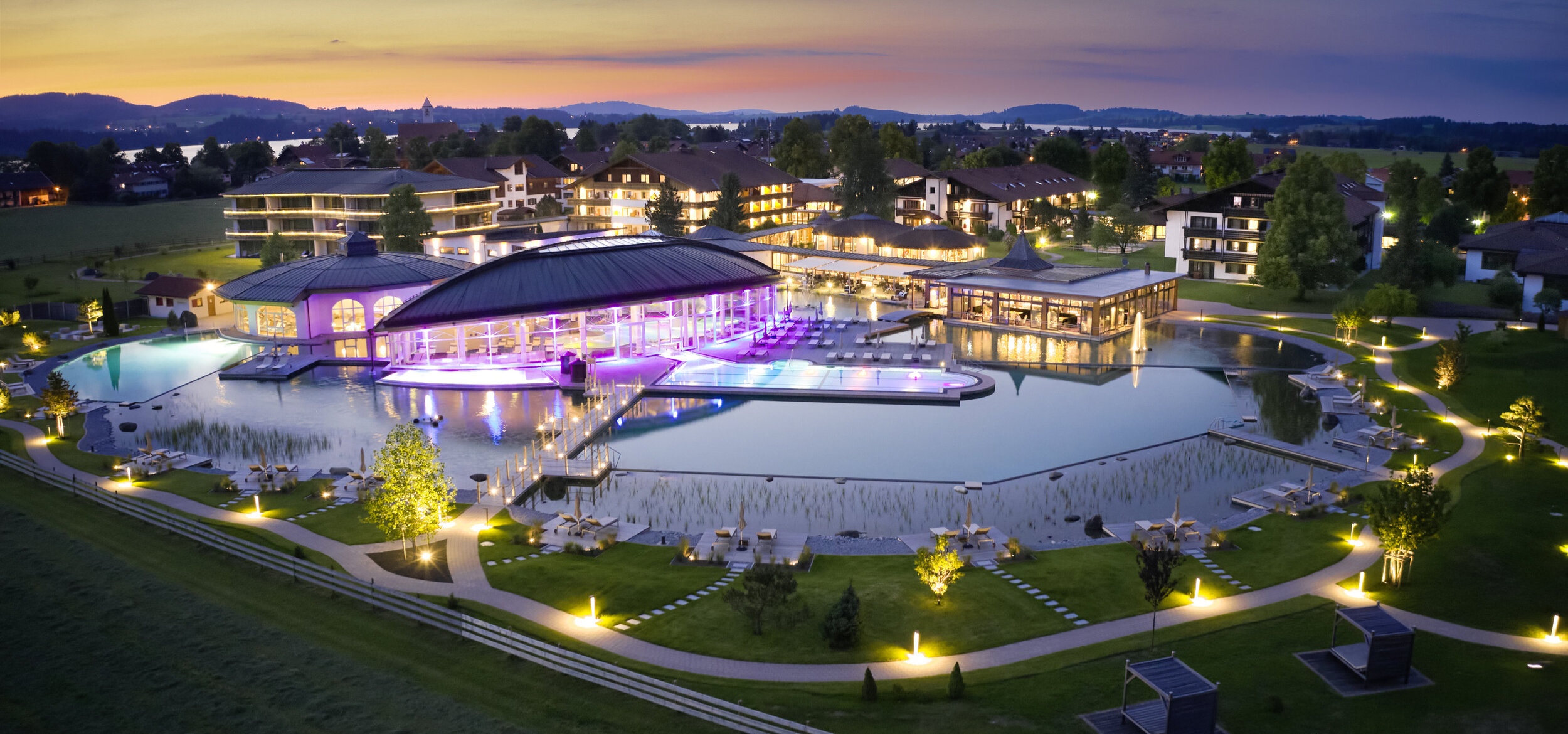 Das „König Ludwig” Wellness & SPA Resort Allgäu in Schwangau in den Abendstunden mit eingeschalteter Beleuchtung & beleuchtetem Pool