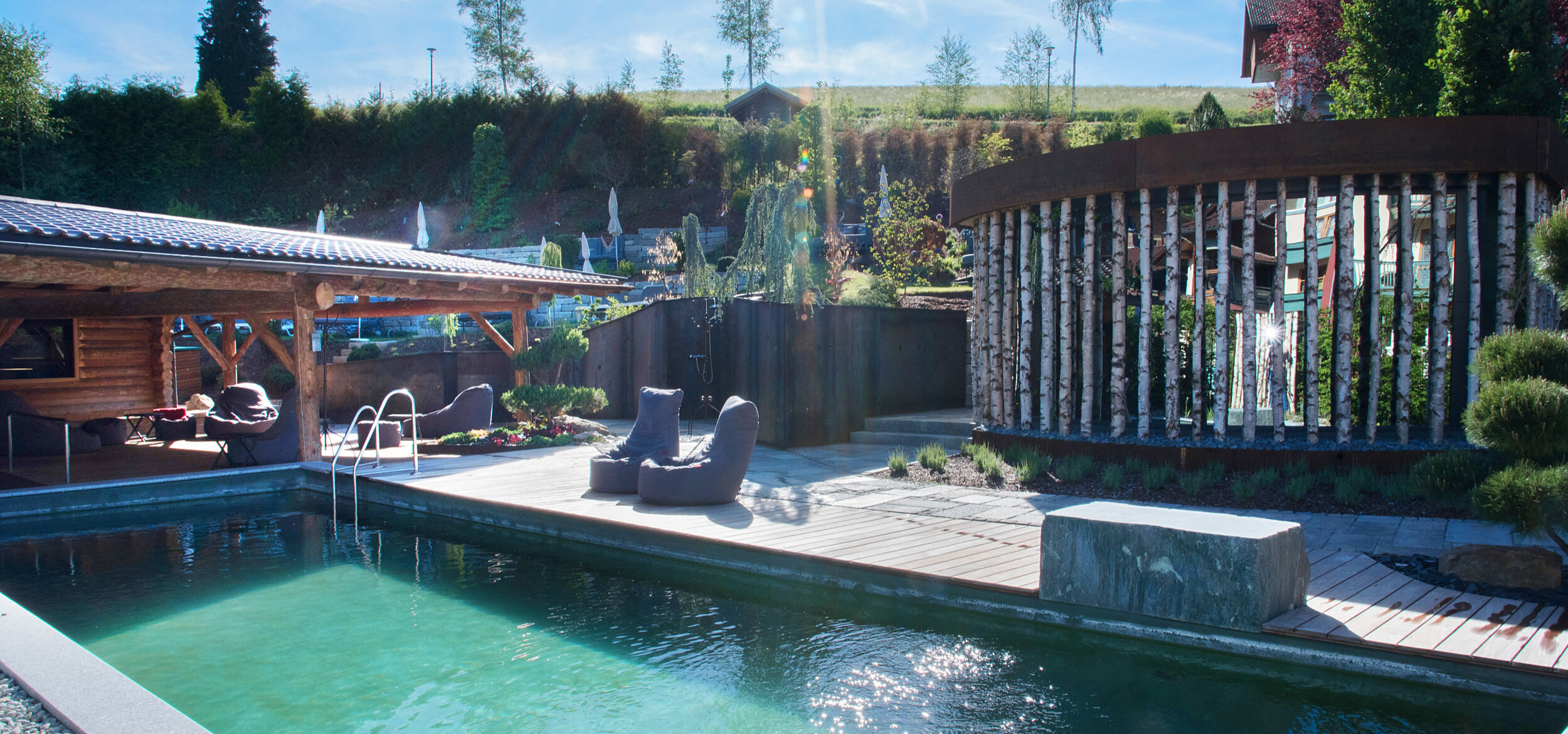 Der Naturpool mit Balena-System im FKK-Bereich des Wellness- & Familienhotel „Zum Kramerwirt" in Geiersthal, im Hinterrund Schirme und Liegen
