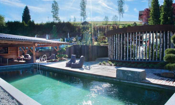 Der Naturpool mit Balena-System im FKK-Bereich des Wellness- & Familienhotel „Zum Kramerwirt" in Geiersthal, im Hinterrund Schirme und Liegen