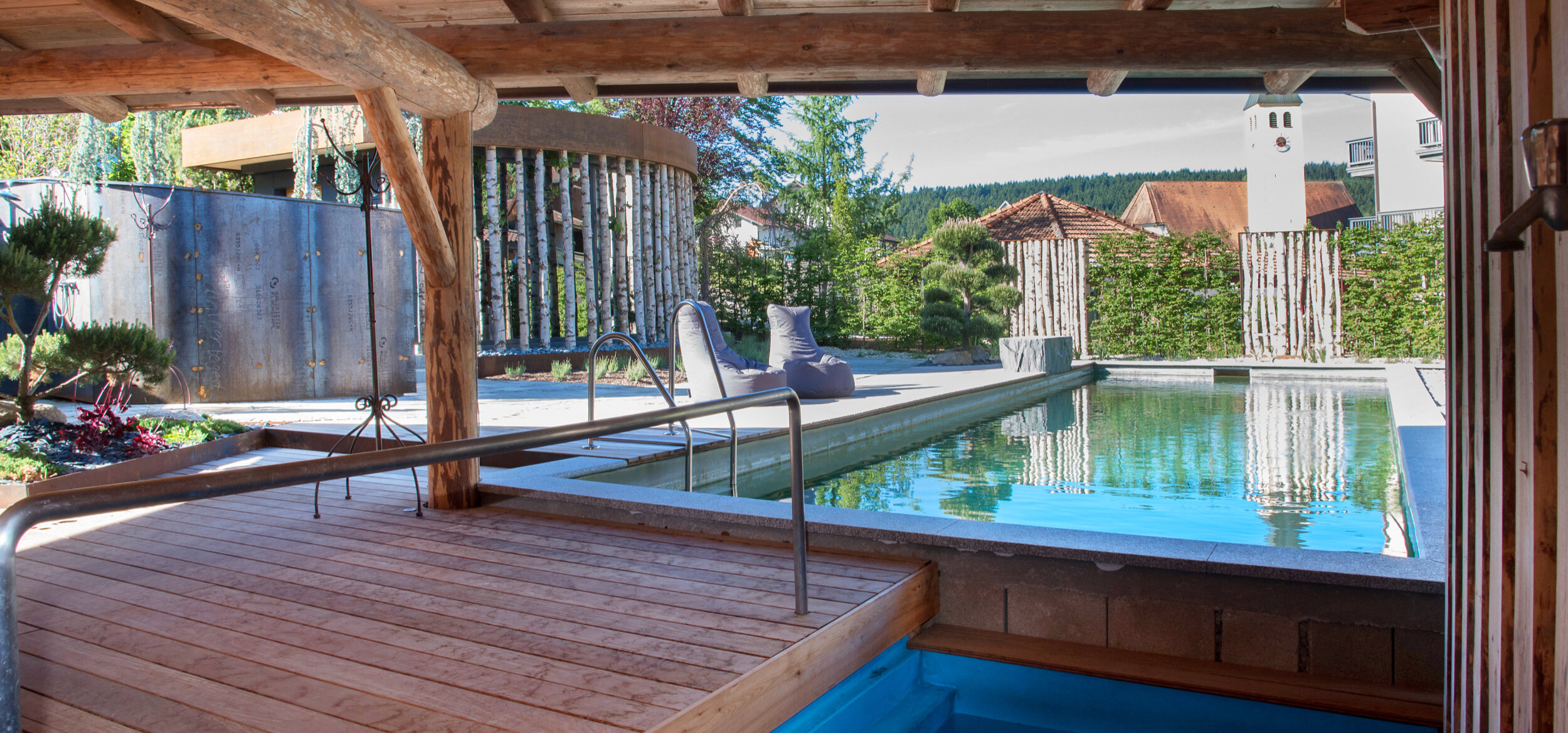 Der Außenbereich des Wellness- & Familienhotel „Zum Kramerwirt" mit Whirlpool und Überdachung, im Hintergrund der Balena-Naturpool mit Sitzmöglichkeiten