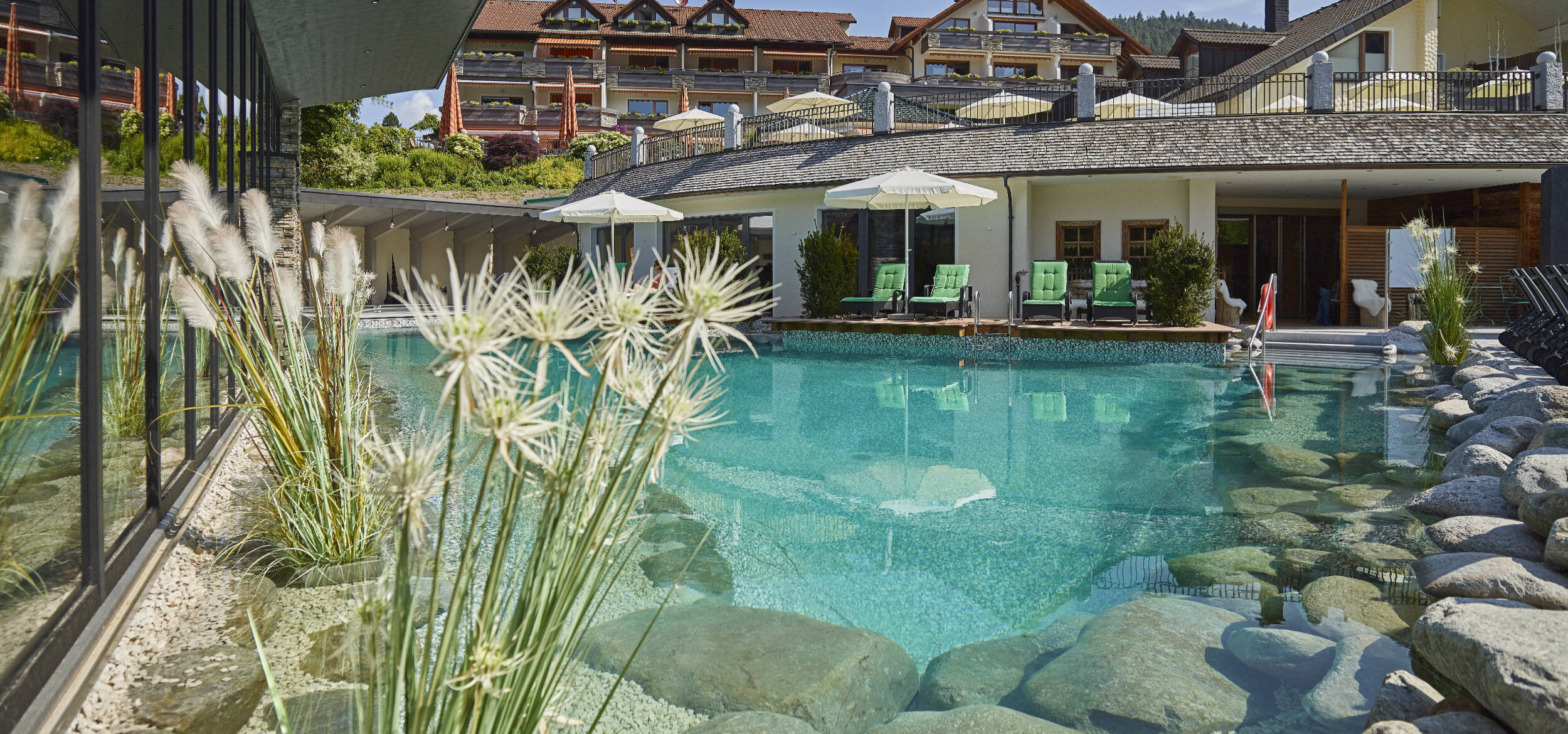 Naturbadeteich mit Balena-System im Wellnesshotel „Heselbacher Hof” in Baiersbronn mit Begrünung und Steinen am Rand, im Hintergrund Liegestühle
