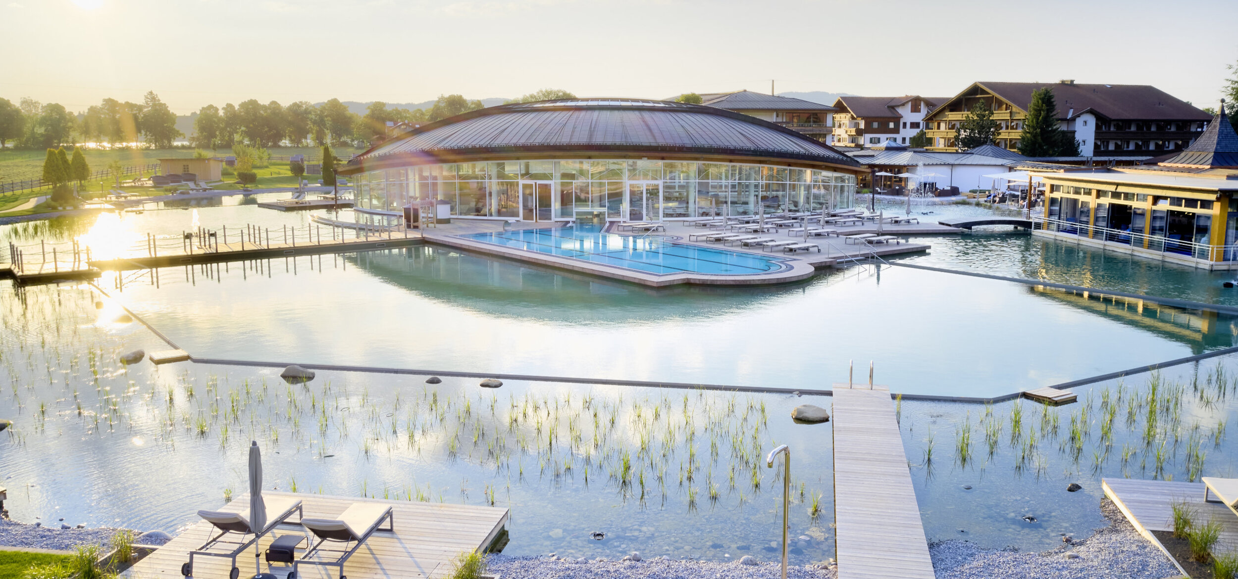 Die Poollandschaft mit Balena-System des „König Ludwig” Wellness & SPA Resort mit Badeliegen und Bepflanzung